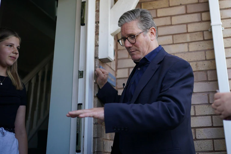 Keir Starmer speaking to a young woman on the threshold of her home.