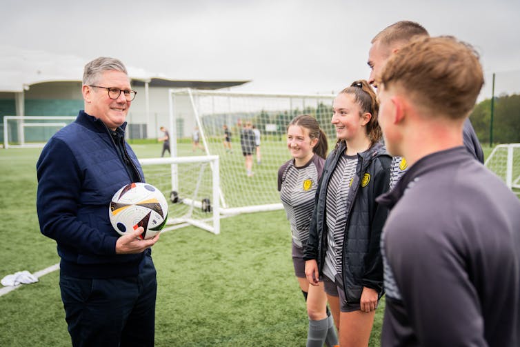 Keir Starmer holding a football and talking to some young people.