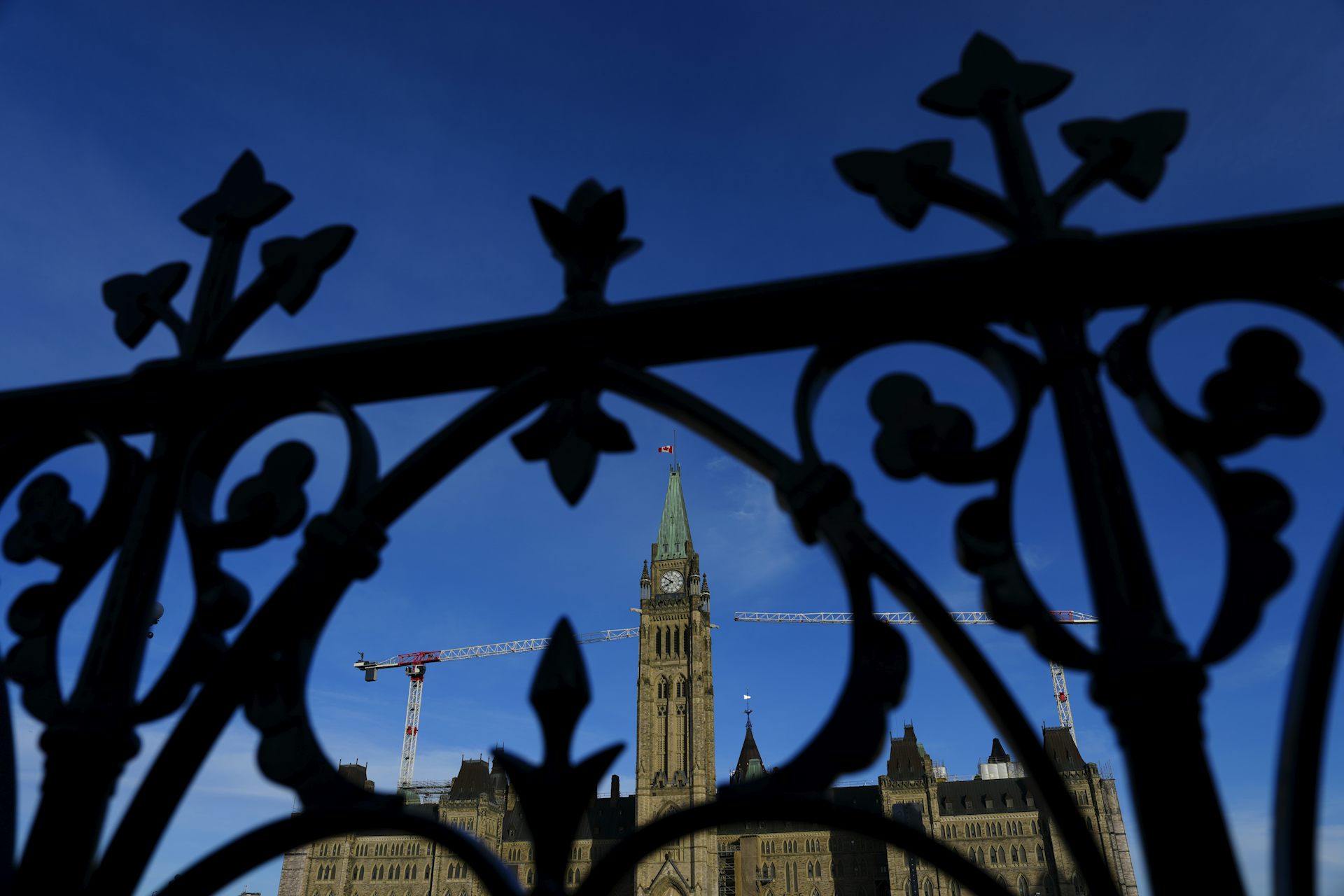 The Peace Tower in Parliament Hill in morning light behind a wrought-iron fence.