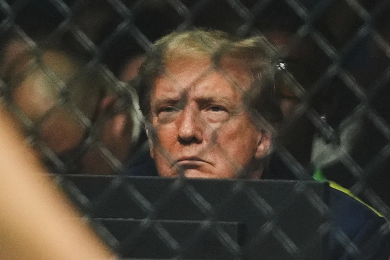 A man with blond hair frowns and is pictured through a chain link barrier.