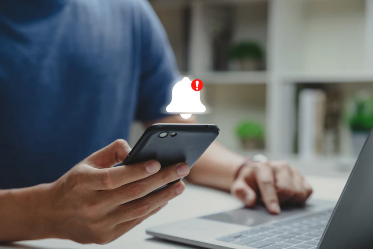 A person holding a smartphone, a graphic of a bell hovers above the phone