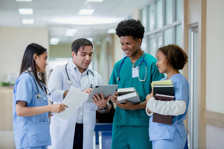 A man in a white coat and stethoscope talking to three young people in scrubs