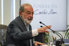A bearded aging man with thinning hair speaks into a microphone.