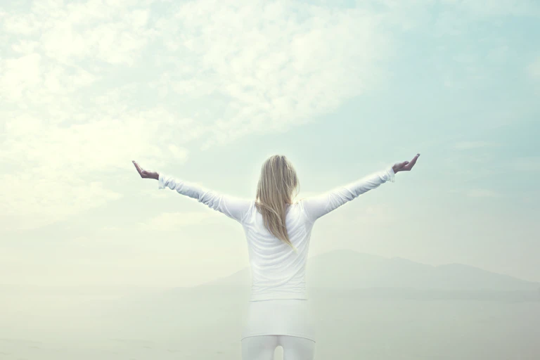 A person stands with arms outstretched in front of a vast sky.