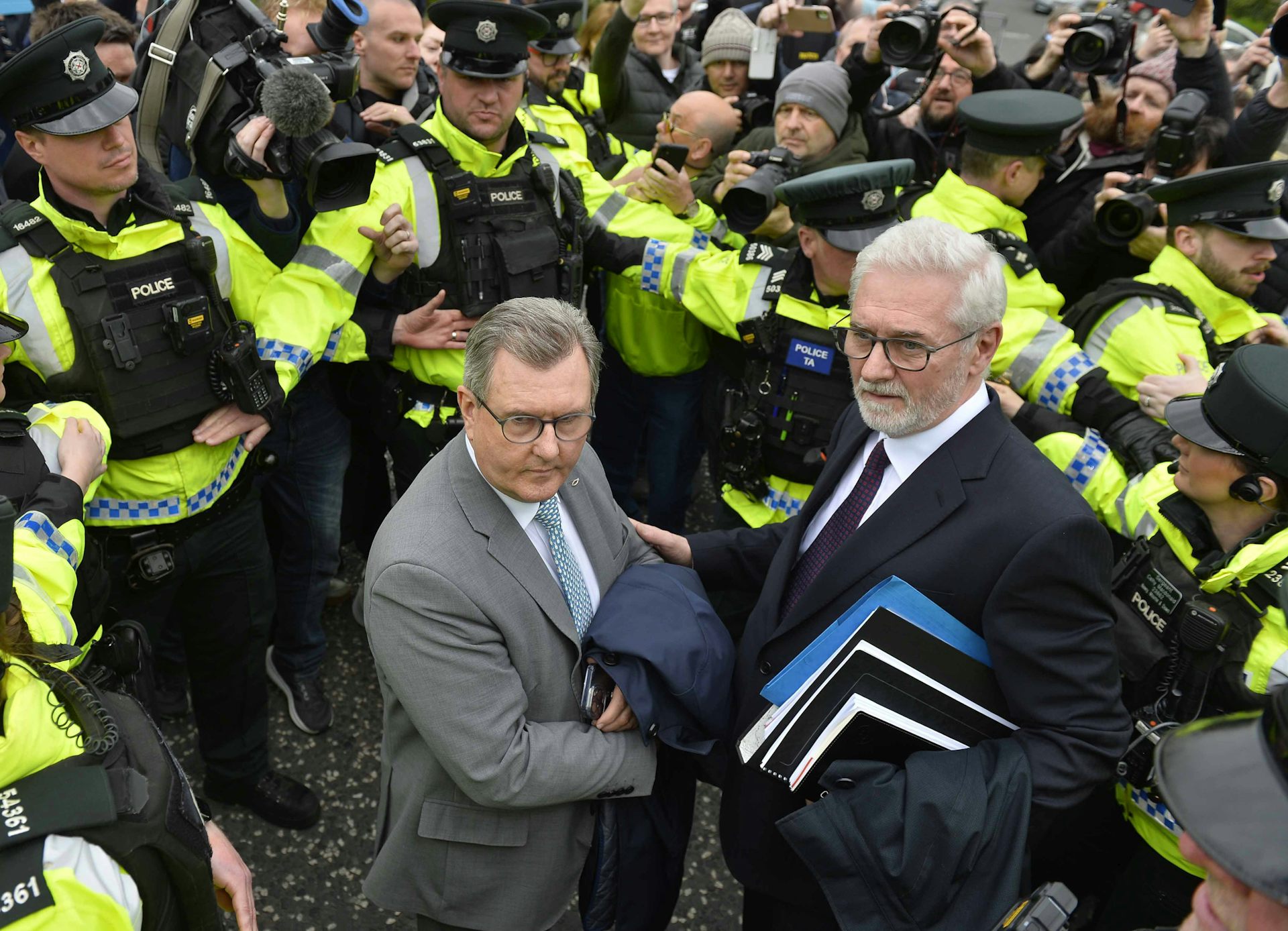 Jeffrey Donaldson e outro homem cercado pela polícia e pela imprensa.