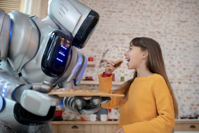 a robot holds a tray of food in front of a girl who is about to take a bite of food she is holding
