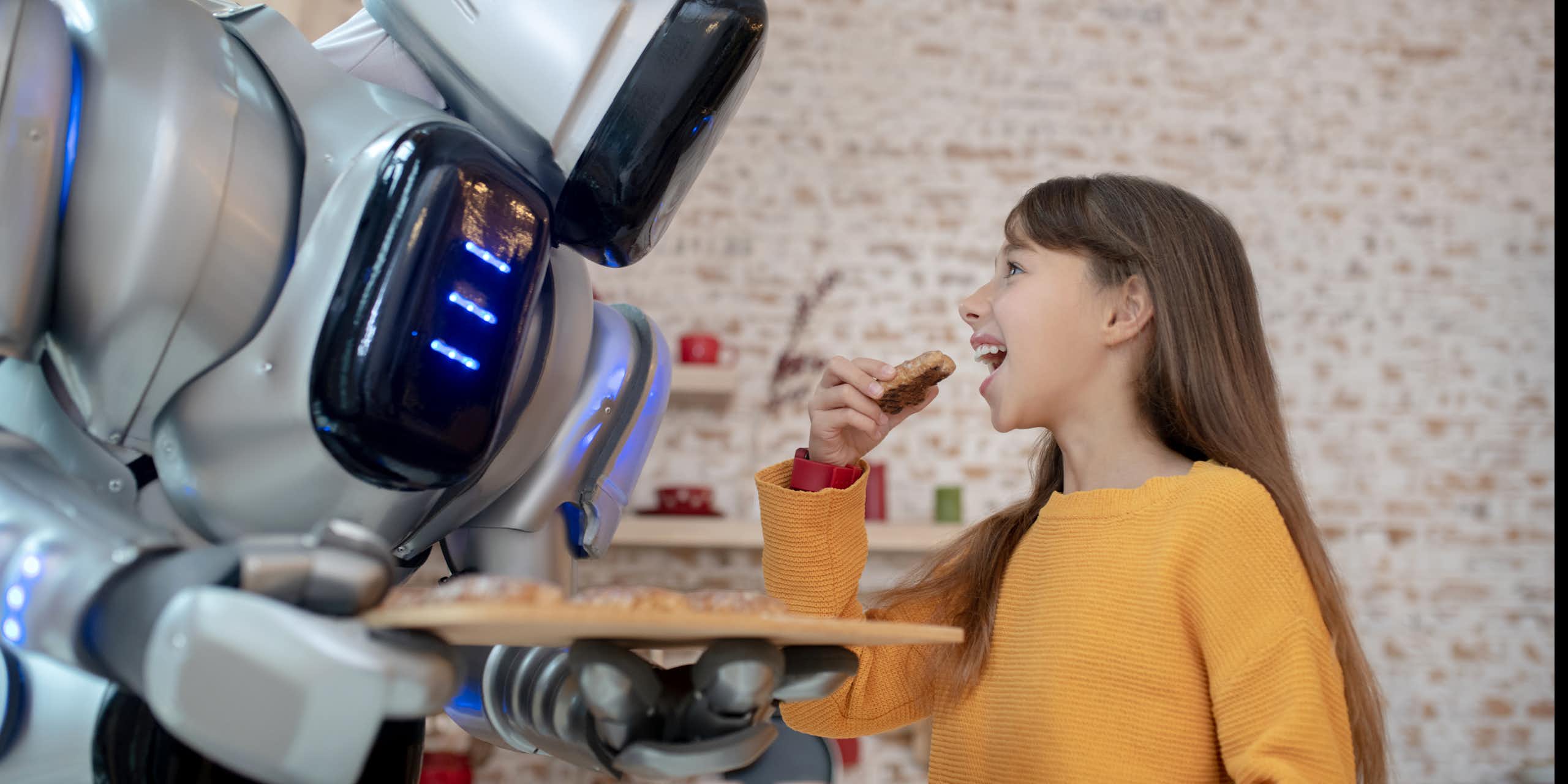 a robot holds a tray of food in front of a girl who is about to take a bite of food she is holding