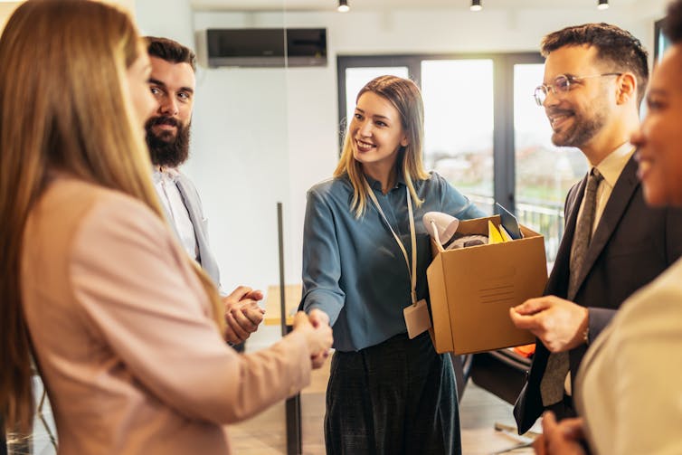 A young woman smiling and shaking hands with another woman as they stand in a group of people