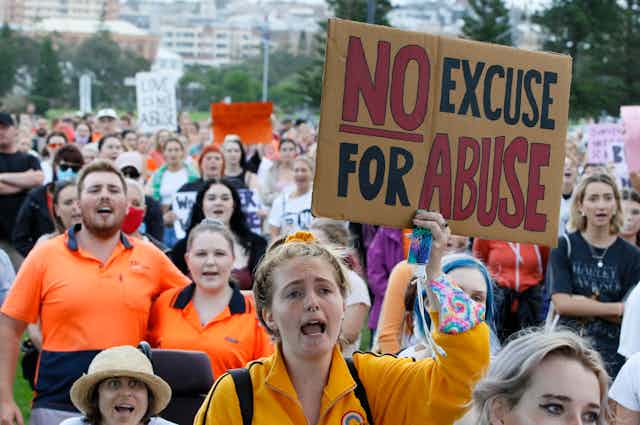 A crowd of people in a rally with a woman holding a sign that says no excuse for abuse.