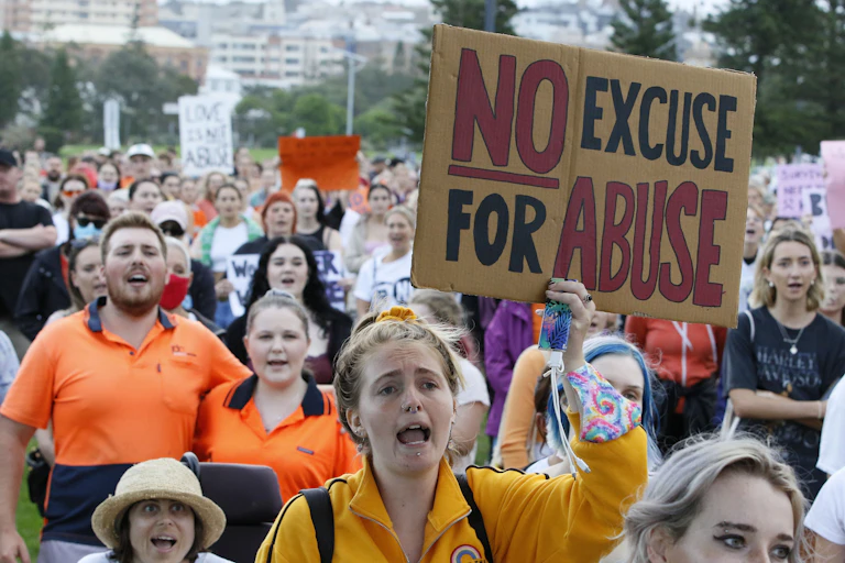 A crowd of people in a rally with a woman holding a sign that says no excuse for abuse.
