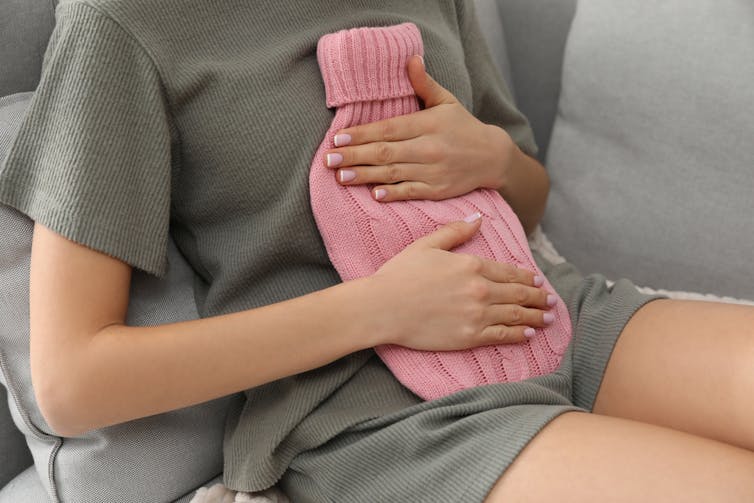 Woman holding hot water bottle (pink cover) on belly
