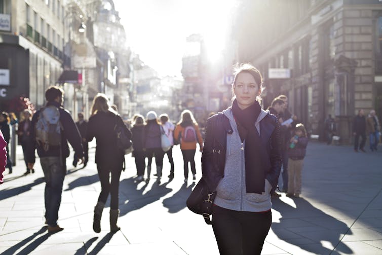 A woman wearing a jacket and scarf walks in a busy European street