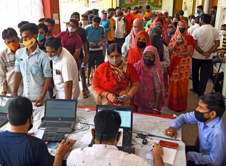 Indian people wearing masks as they queue waiting to be vaccinated against COVID.