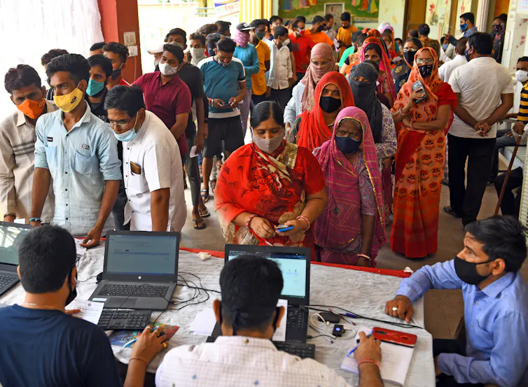 Indian people wearing masks as they queue waiting to be vaccinated against COVID.