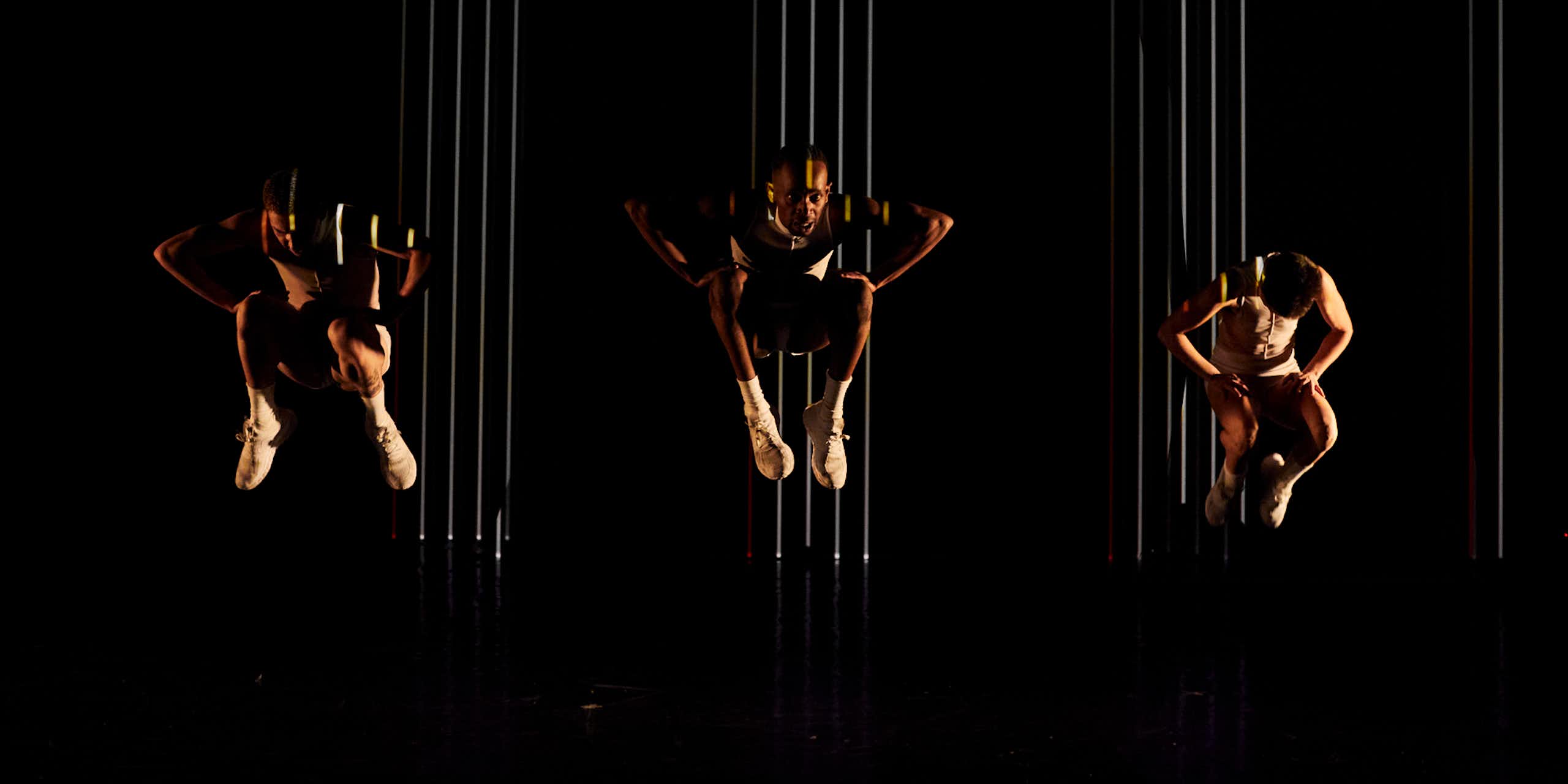 Three dancers against a black backdrop, suspended in the air.