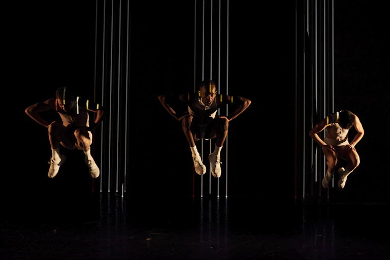 Three dancers against a black backdrop, suspended in the air.