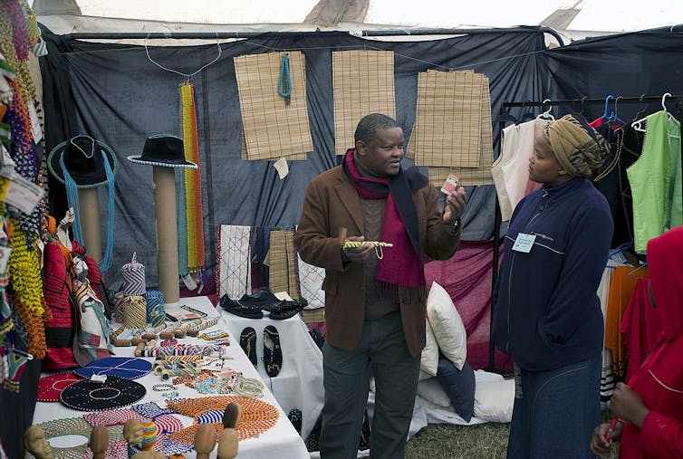 A market stall, a man talking to a woman surrounded by a display of craft.