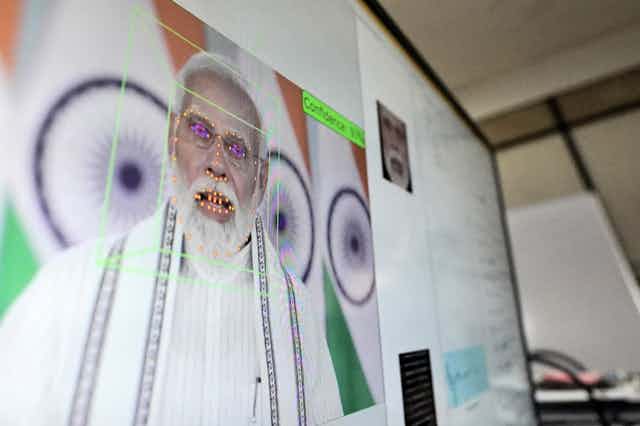 a computer screen shows a man with white hair and beard in front of oragne, green and white flags with a series of bright dots outlining his mouth, nose and eyes