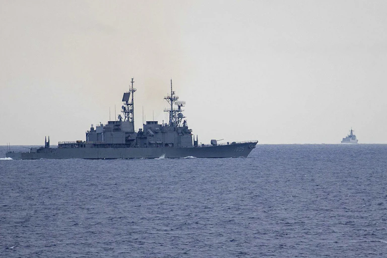 Two military destroyers, one further off on the horizon.