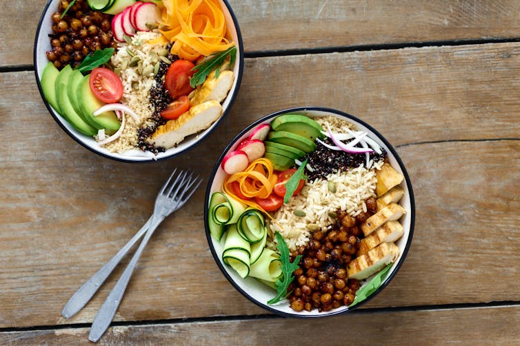 Two bowls of food on a table, containing grilled chicken, rice, legumes, and colourful vegetables.