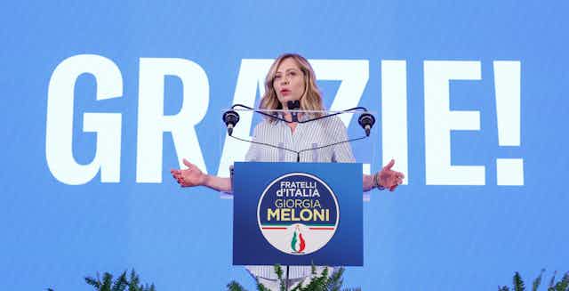 Georgia Meloni delivering a speech in front of a sign reading "Grazie".