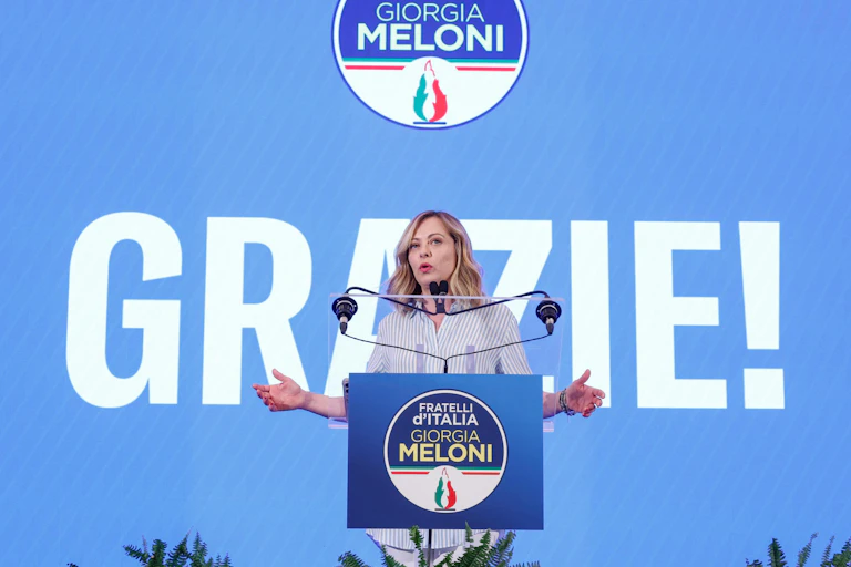 Georgia Meloni delivering a speech in front of a sign reading "Grazie".