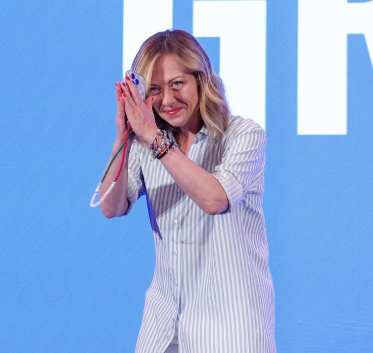 Georgia Meloni está com as mãos entrelaçadas saudando a multidão.