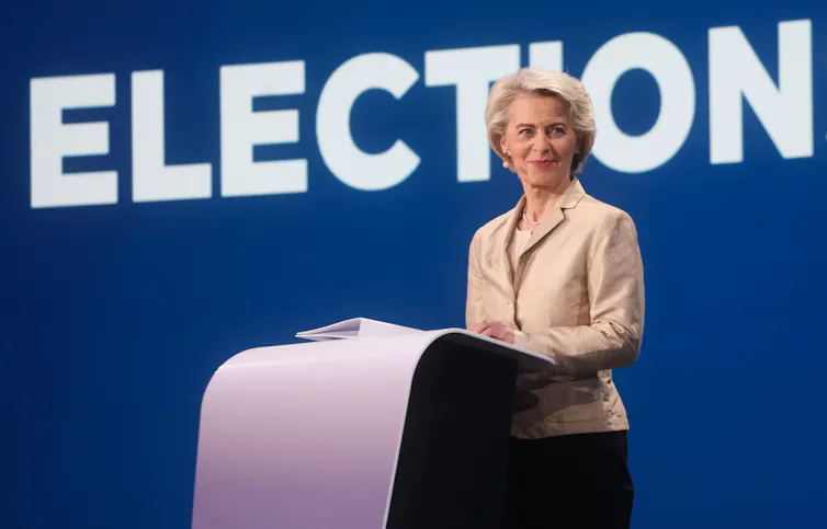 Von der Leyen standing at a podium in front of a sign reading