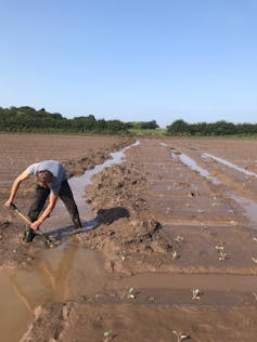 A farmer shovelling in a muddy field.