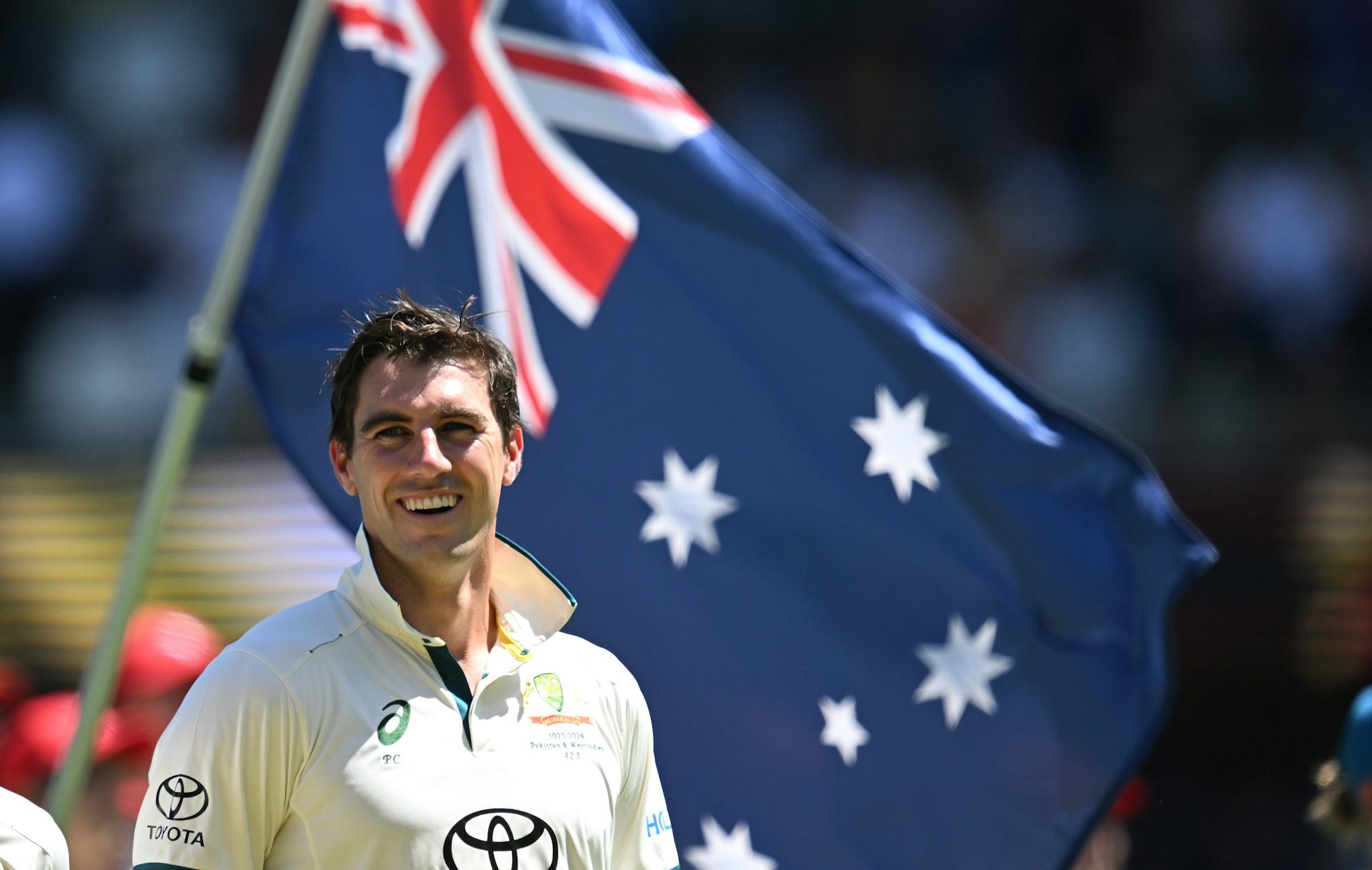 Pat Cummins smiling as an Australia flag is waved in the background.