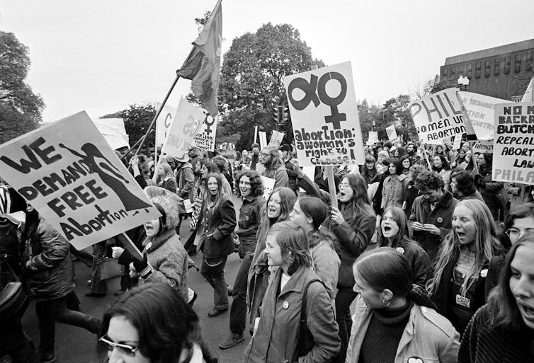A black and white photo shows a large crowd of people with signs and flags.