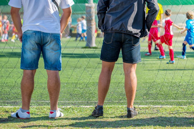 Two unidentified spectators watching a children's football match