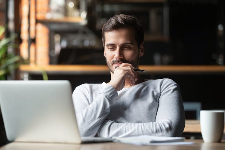 A man sitting at a table looking at a laptop screen