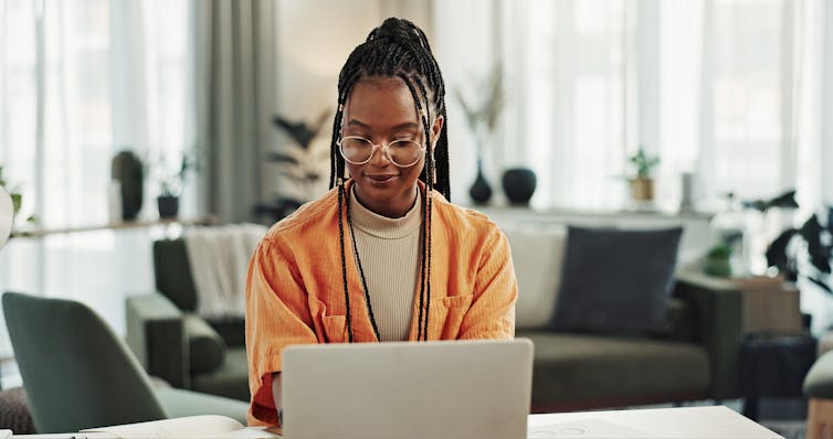 A young woman sitting in a living room working on a laptop