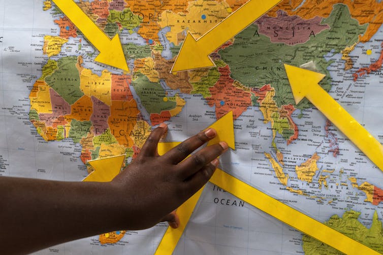 A hand points to a world map with yellow arrows pointing to several countries.