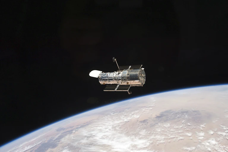 The Hubble telescope, which looks like a metal cylinder with solar panels attached, floating above Earth.