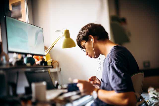 young man sits at computer with headphones on