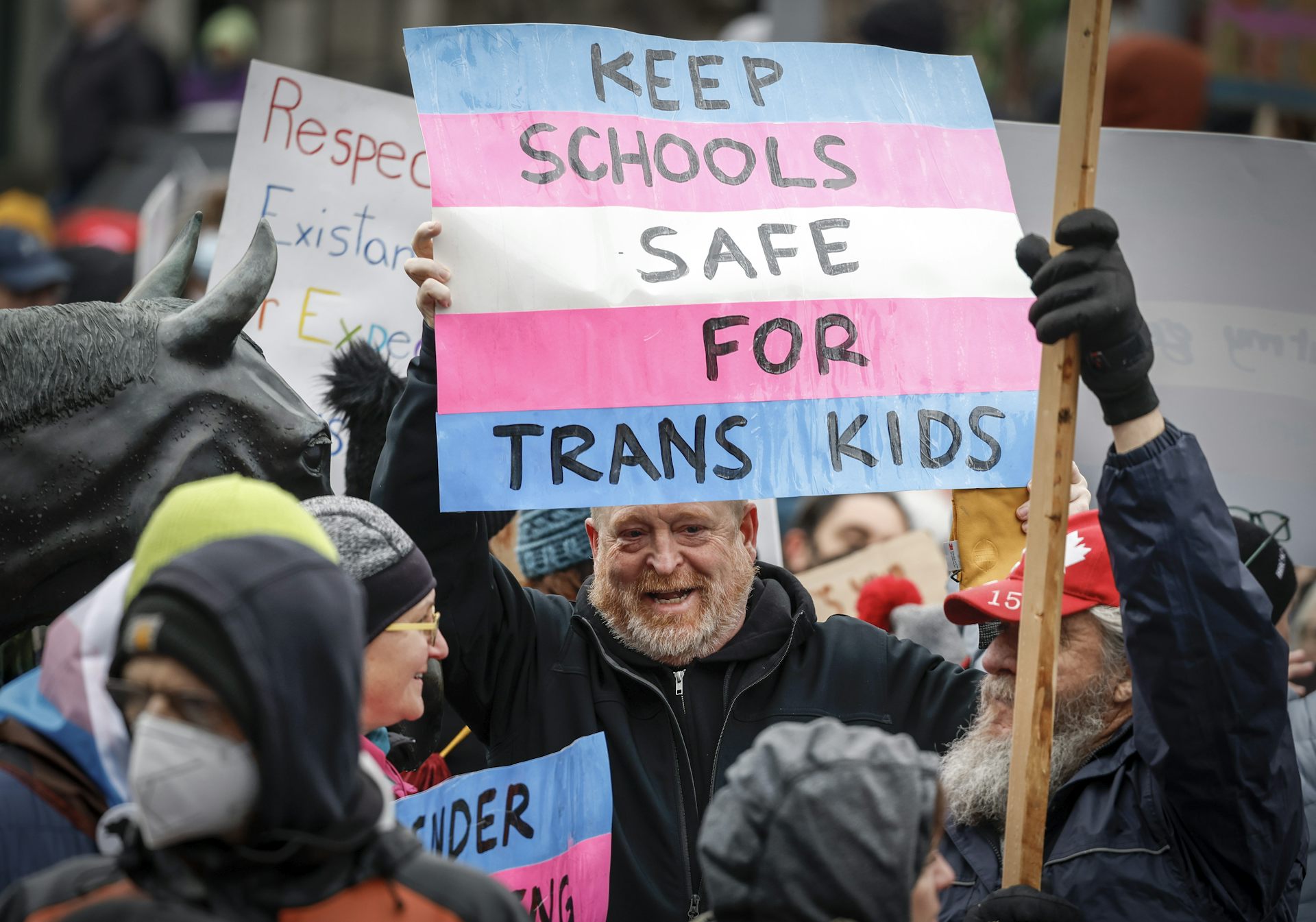 A man at a rally carries a sign reading: keep schools safe for trans kids