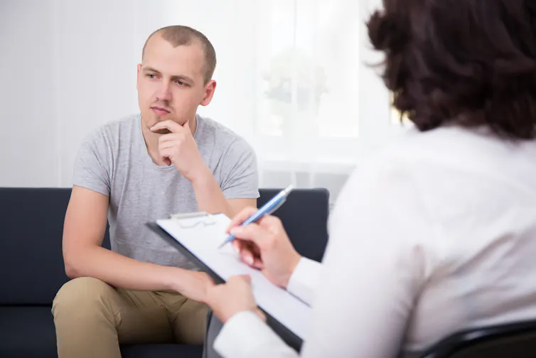 A young man looks thoughtful while a doctor writes on a clipboard.