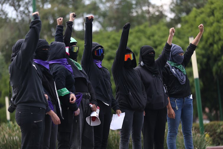 A group of women dressed in black with covered faces holding a clenched fist above their heads.