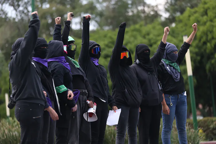A group of women dressed in black and with their faces covered holding a clenched fist above their heads.