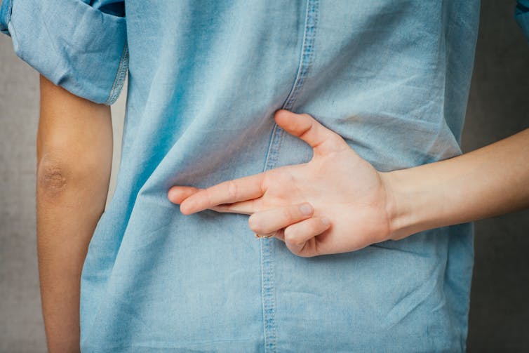 Pessoa cruza os dedos atrás das costas