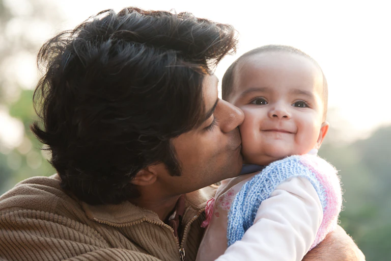 A father kissing his baby's cheek and the baby looks proud and happy..