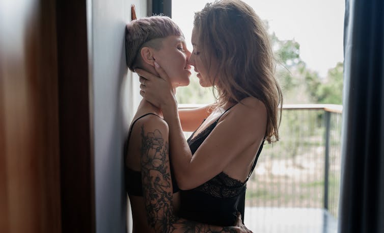 Two women, one with short hair and one with long hair, stand nose to nose against a door