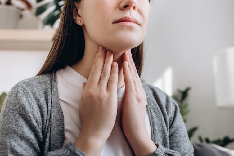 A woman tenderly touches her throat with both hands