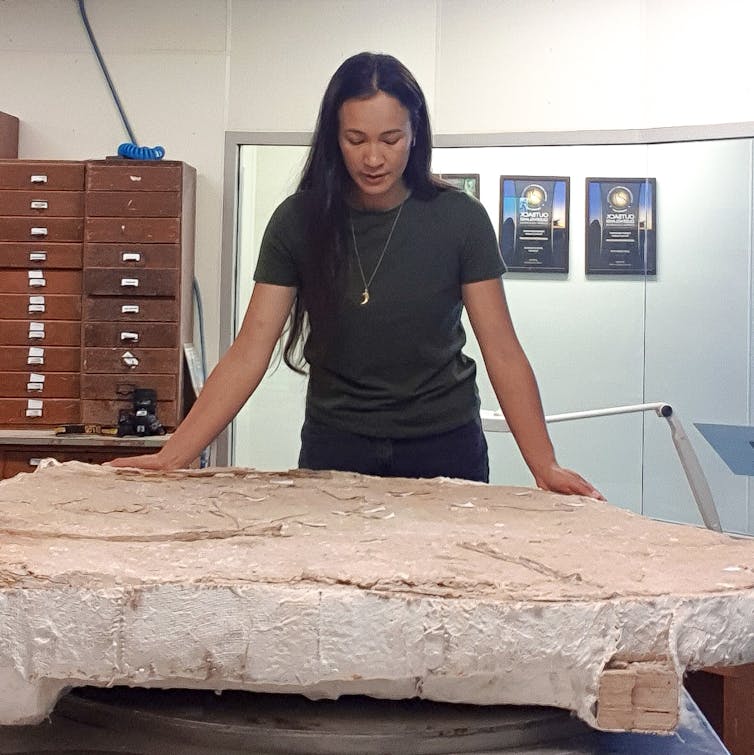 Photo of a woman inspecting a slab of rock in a laboratory.