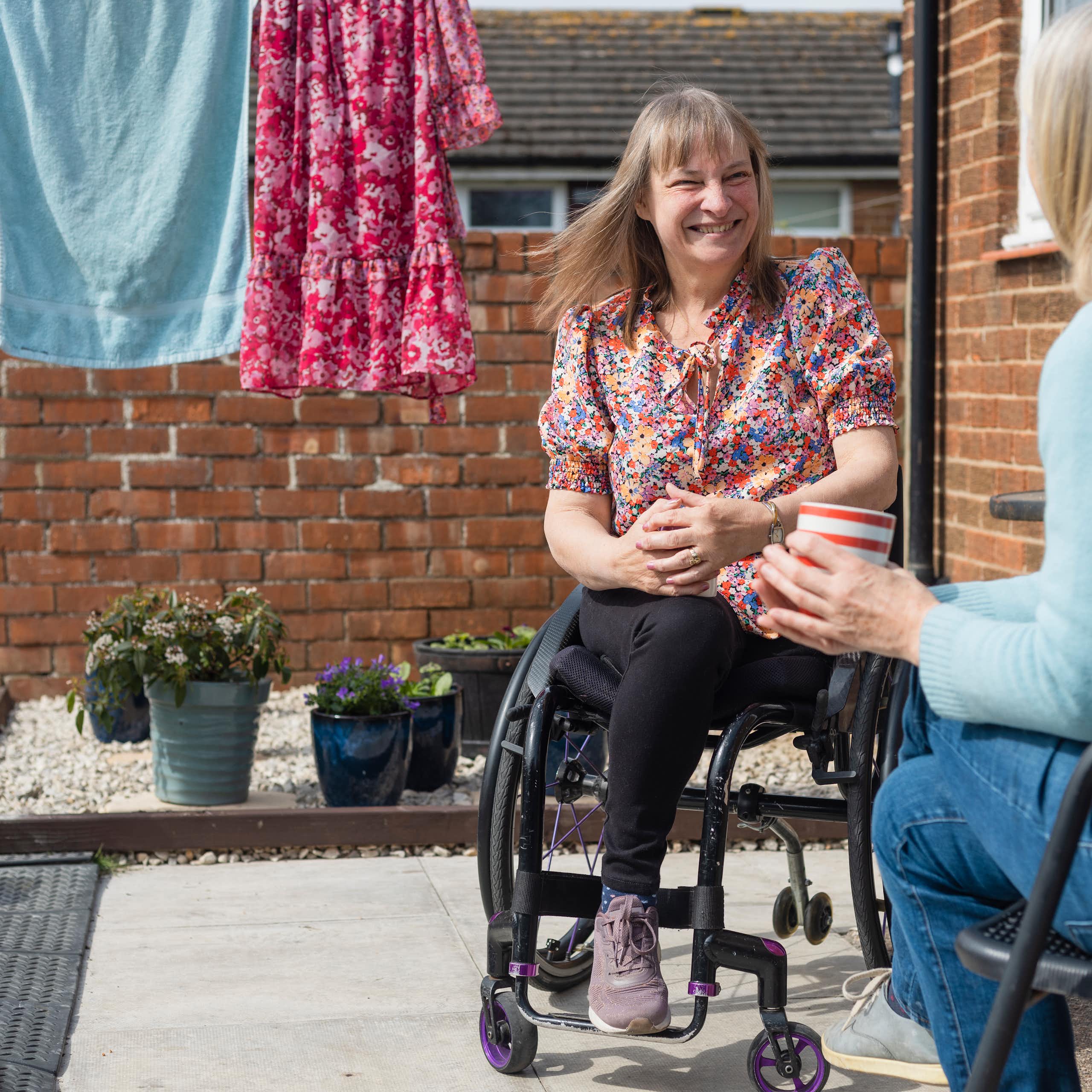 two women talking in home courtyard with washing hanging nearby. One woman using wheelchair