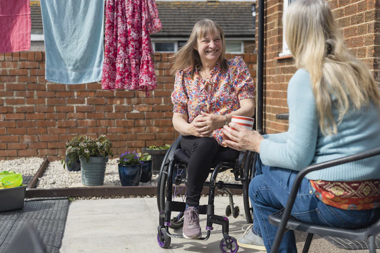 two women talking in home courtyard with washing hanging nearby. One woman using wheelchair