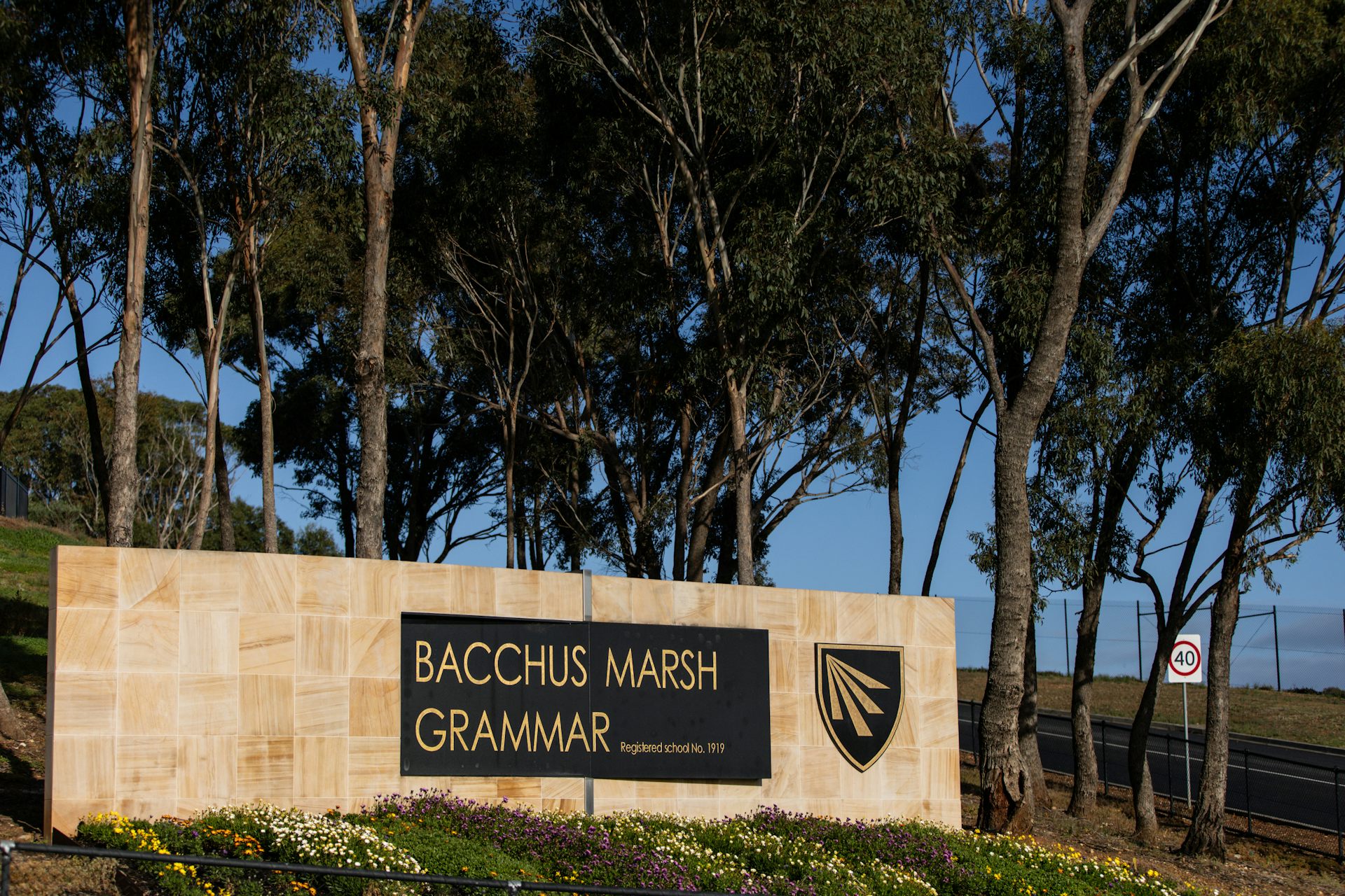A sandstone sign for Bacchus Marsh Grammar in front of established trees and next to a road.