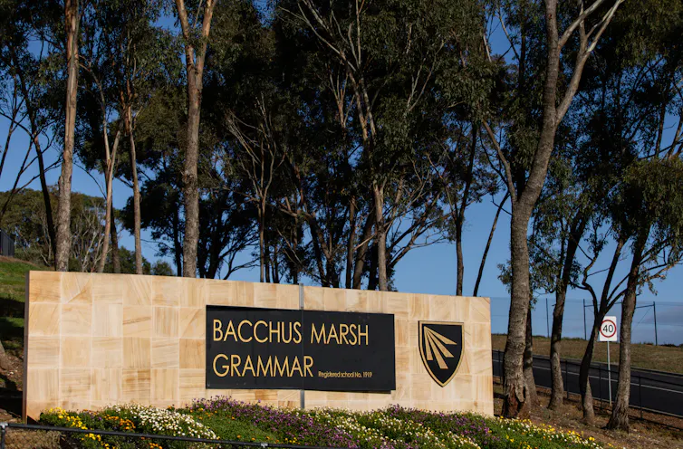 A sandstone sign for Bacchus Marsh Grammar in front of established trees and next to a road.